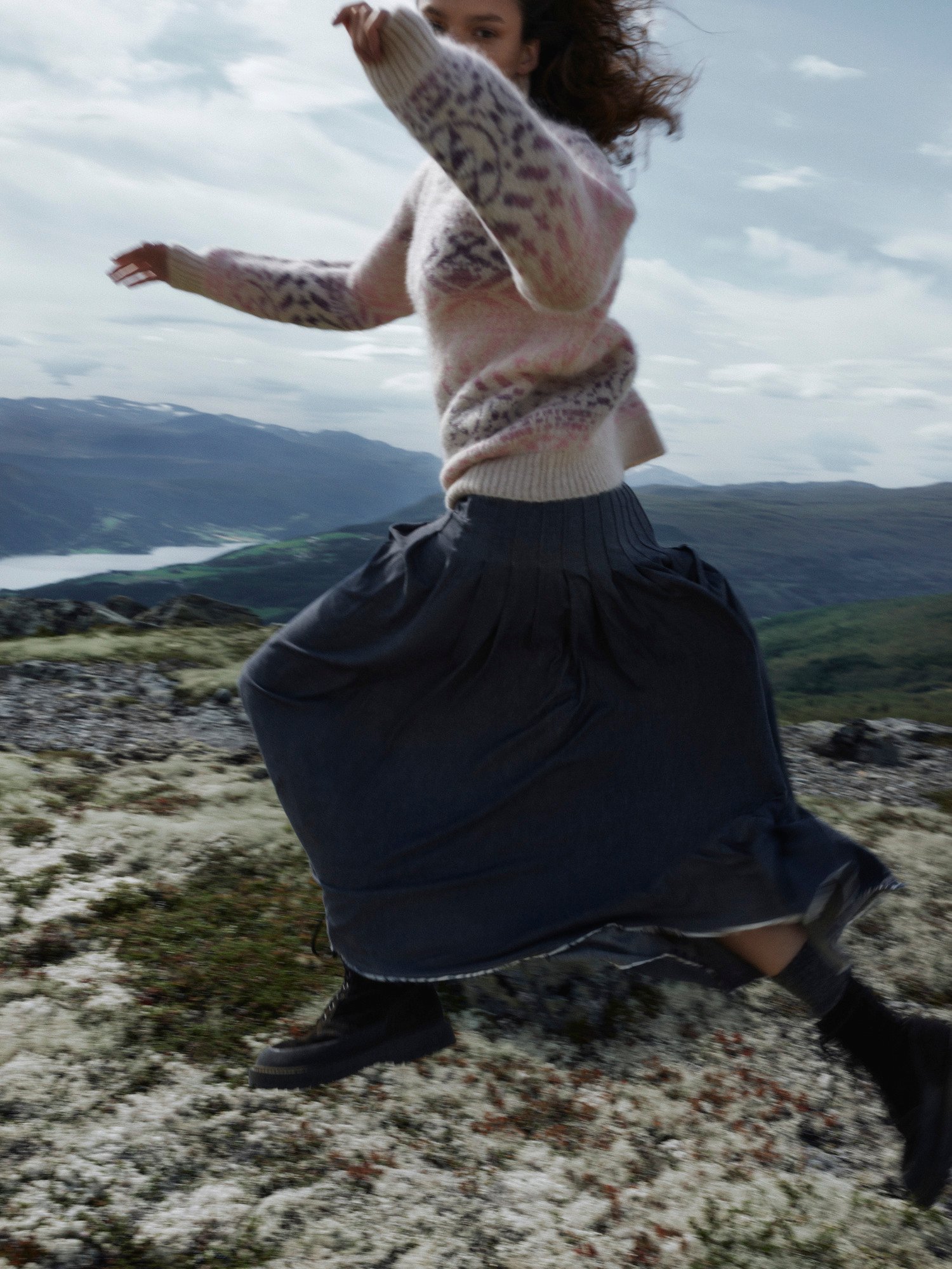 Kvinnelig modell hopper i norsk natur med rosa Highland strikket genser fra Dale of Norway
